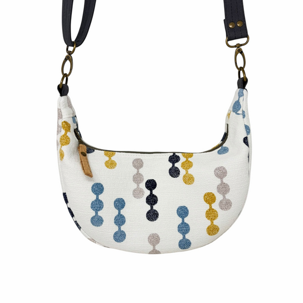 mmb by hand crescent crossbody bag in white textured fabric with navy, mustard, and grey geometric dot pattern.